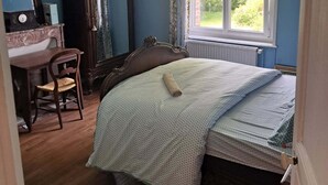 A bedroom with a bed, a dresser, a chair, a large mirror, and a window with a view of greenery.