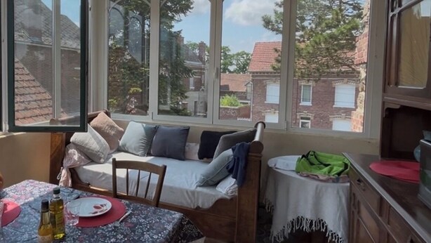 A cozy room with a sofa, a dining table, and a view of a brick building through large windows.