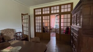 A room with a dining table, chairs, a wooden cabinet, and a large window with a view of the outside.