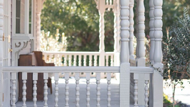 A white porch with a chandelier, a bench, and a view of trees. - The Gilded Lady-King bed suite and private balcony (Pensacola)