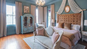 A bedroom with a large bed, a chaise lounge, a wooden headboard, a vintage armoire, and a chandelier. - The Gilded Lady-King bed suite and private balcony (Pensacola)