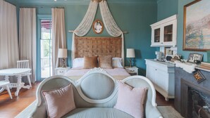 A bedroom with a large bed, a chandelier, a white dresser, and a fireplace. - The Gilded Lady-King bed suite and private balcony (Pensacola)