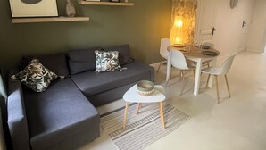 En moderne stue med en grå hjørnesofa, et lille hvidt bord og et spiseområde med en væg i natursten og en hængende lampe.