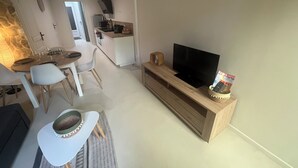En moderne stue med spiseplads, et køkken og et fjernsyn på et træstel.