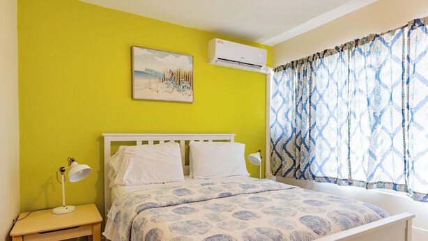 Een slaapkamer met een bed, nachtkastjes, een wandairconditioner en een raam met gordijnen met een patroon.