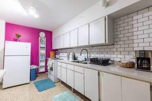 Eine kleine Küche mit weißen Schränken, einem weißen Kühlschrank, einer Spüle mit Armatur und einer Kaffeemaschine.