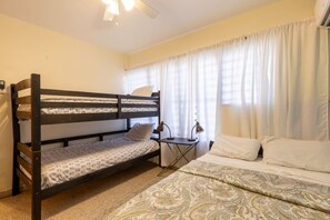 Ein Schlafzimmer mit Etagenbett, einem Einzelbett, einem Schreibtisch mit Lampe und einem Fenster mit Vorhängen.