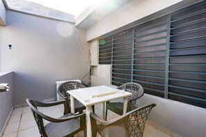 Ein kleiner Balkon mit Sitzgelegenheit, einem Fenster mit Jalousien und einer Wand-Klimaanlage.