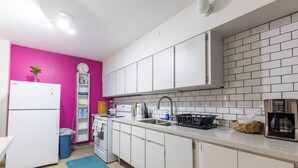 Een keuken met witte kastjes, een roze muur, een witte koelkast, een spoelbak en een koffiezetapparaat.