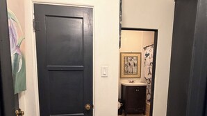 A hallway with a black door, a small bathroom with a toilet and sink, and a framed picture on the wall. - Cozy studio in Lancaster (Lancaster)