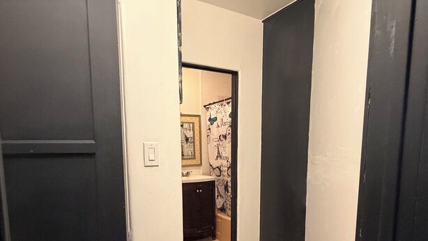A narrow hallway with a wooden floor, a black door on the left, and a bathroom visible in the background. - Cozy studio in Lancaster (Lancaster)