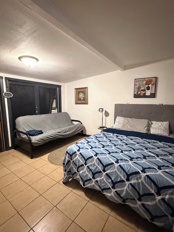 A bedroom with a bed, a sofa, a nightstand, and a wall-mounted lamp.