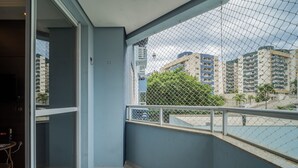 Un balcon avec une rambarde en treillis métallique, une vue sur des immeubles de grande hauteur et une porte donnant sur un espace intérieur.