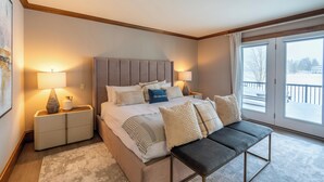 Een moderne slaapkamer met een groot bed, nachtlampjes, een bankje en uitzicht op de natuur.