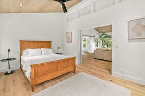 A bedroom with a wooden bed, white bedding, a white rug, and a ceiling fan. - Fresh & Modern 4-bedroom house ~ North Shore Kauai (Princeville)