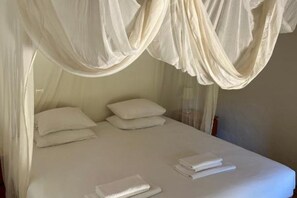 Ein Bett mit weißer Bettwäsche und einem Baldachin.