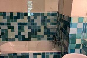 Ein Badezimmer mit Badewanne, gefliesten Wänden und einem Fenster.