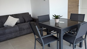 En moderne stue med en grå sofa, et spisebord med glasplade og to stole.