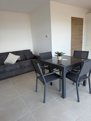 A modern living room with a grey sofa, a glass-top dining table, and two chairs. - L'écrin de Paradis (ALATA)