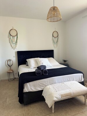 A bed with a dark headboard, white bedding, and a bench at the foot of the bed. - L'écrin de Paradis (ALATA)