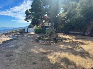 A rustic outdoor area with a stone wall, a wooden deck, and a small garden. - L'écrin de Paradis (ALATA)