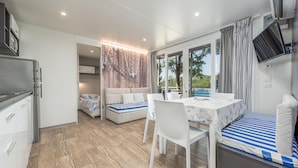 Una habitación moderna y luminosa con una mesa de comedor, sillas blancas y un sofá con cojines a rayas. Un ventanal ofrece vistas al exterior.