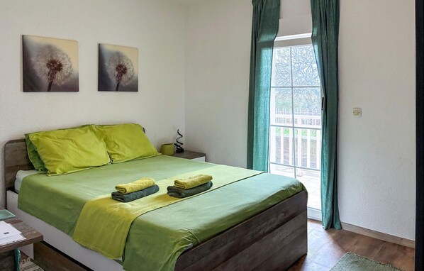 A neatly made bed with green bedding and two towels, a bedside table with a lamp, and two wall-mounted paintings of dandelions.