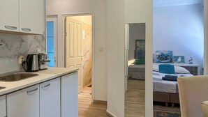 Une cuisine moderne avec des meubles blancs et un pare-feu en marbre, qui donne sur une chambre à coucher équipée d’un lit, d’oreillers et d’un tableau.