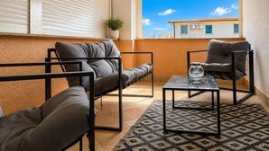 Un balcon avec un canapé, un fauteuil et une table basse, un pot de fleurs et une vue sur les immeubles.