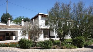 A two-story house with a tiled roof, a balcony, and a garden with various plants and flowers. - Cozy 1-Bedroom Apartment with Terrace and Pool in Bensafrim (Bensafrim)