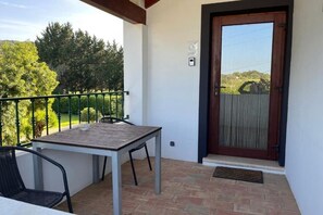 Ein Balkon mit Tisch und Stühlen, eine Holztür und Blick auf Bäume und Hügel.