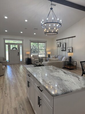 A spacious kitchen with a marble island, a chandelier, and a large window providing natural light. - Great get away central to Orlando, Ocala, The Villages family friendly (Sumterville)