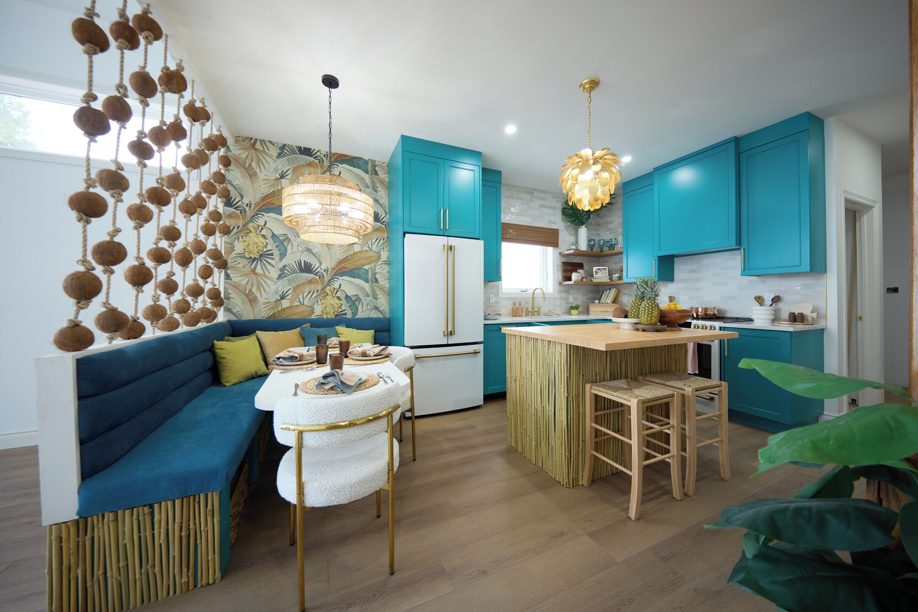 A modern kitchen with teal cabinets, a central island, and a dining area with a blue sofa and white table.