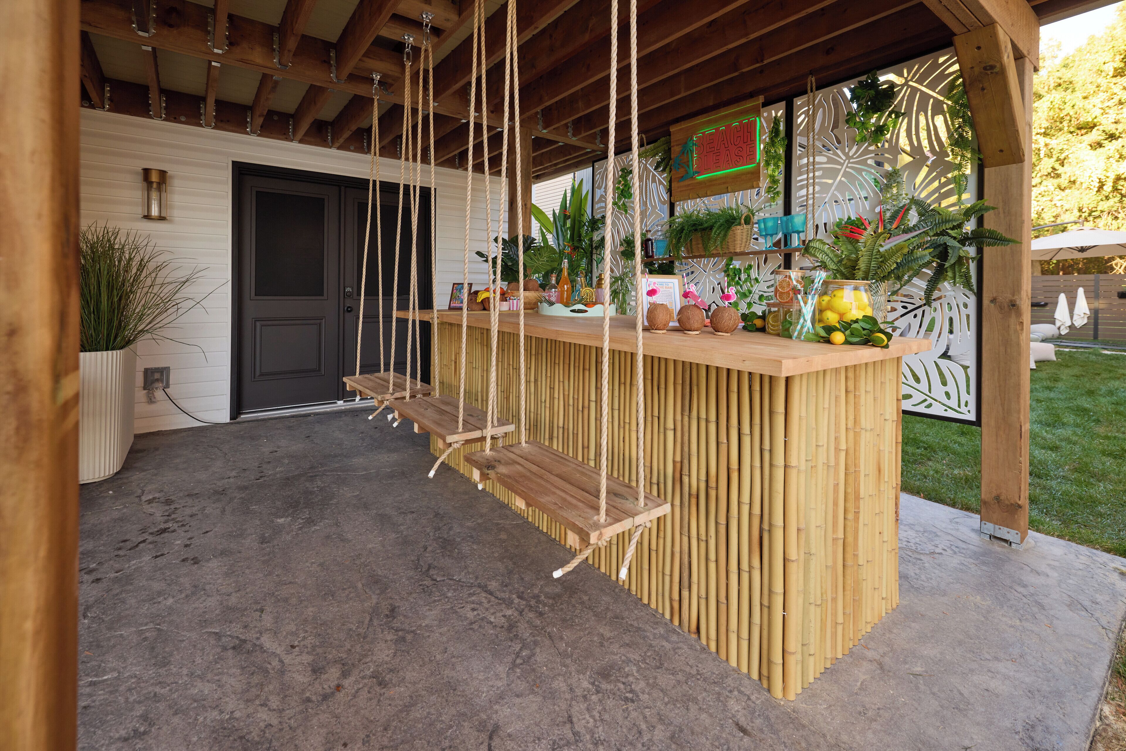 Un espace extérieur abrité avec des sièges, une balançoire en bois et un bar en bambou.