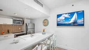 A modern kitchen with white cabinetry, a central island with chairs, a microwave, and a refrigerator.