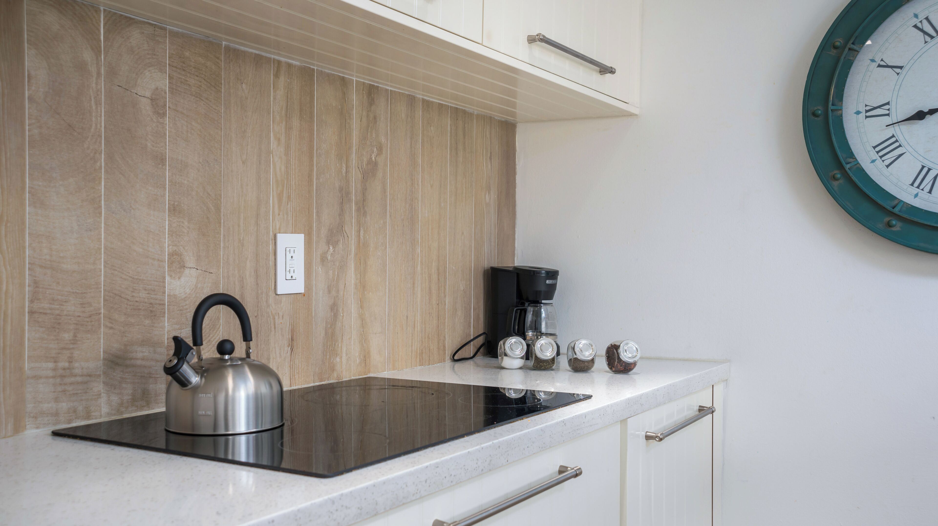 A kitchen with a stainless steel kettle, a coffee maker, and salt and pepper shakers on the counter.