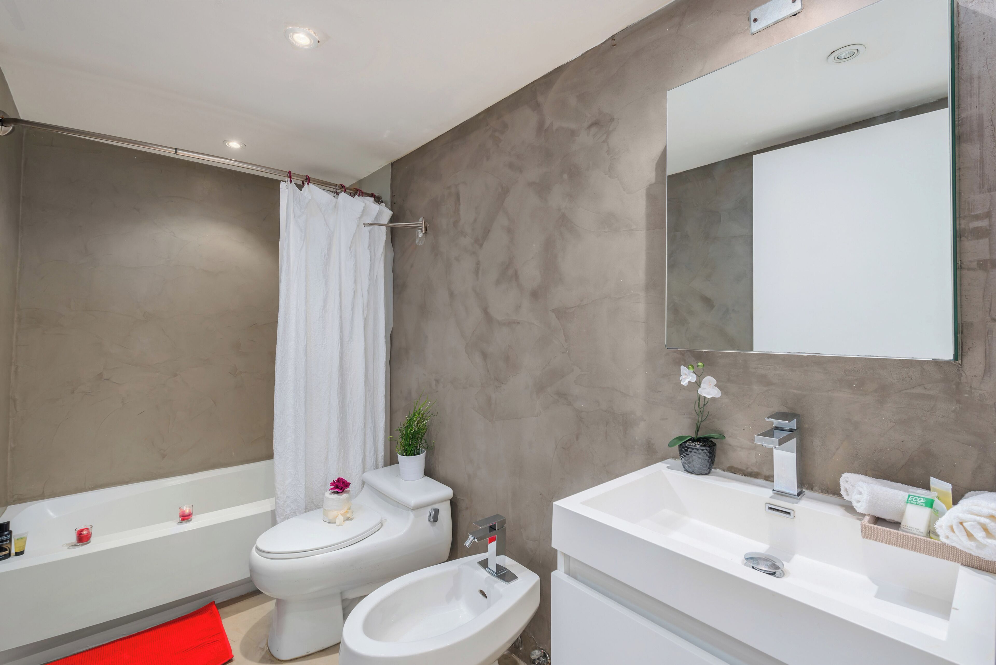 Un baño moderno con bañera, inodoro, bidé y un espejo grande.