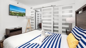 A hotel room with a bed, a TV mounted on the wall, a nightstand, a lamp, and a sliding door closet.