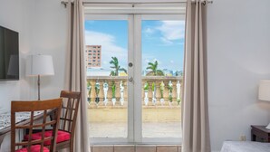 A hotel room with a sliding glass door leading to a balcony with a view of palm trees and buildings.