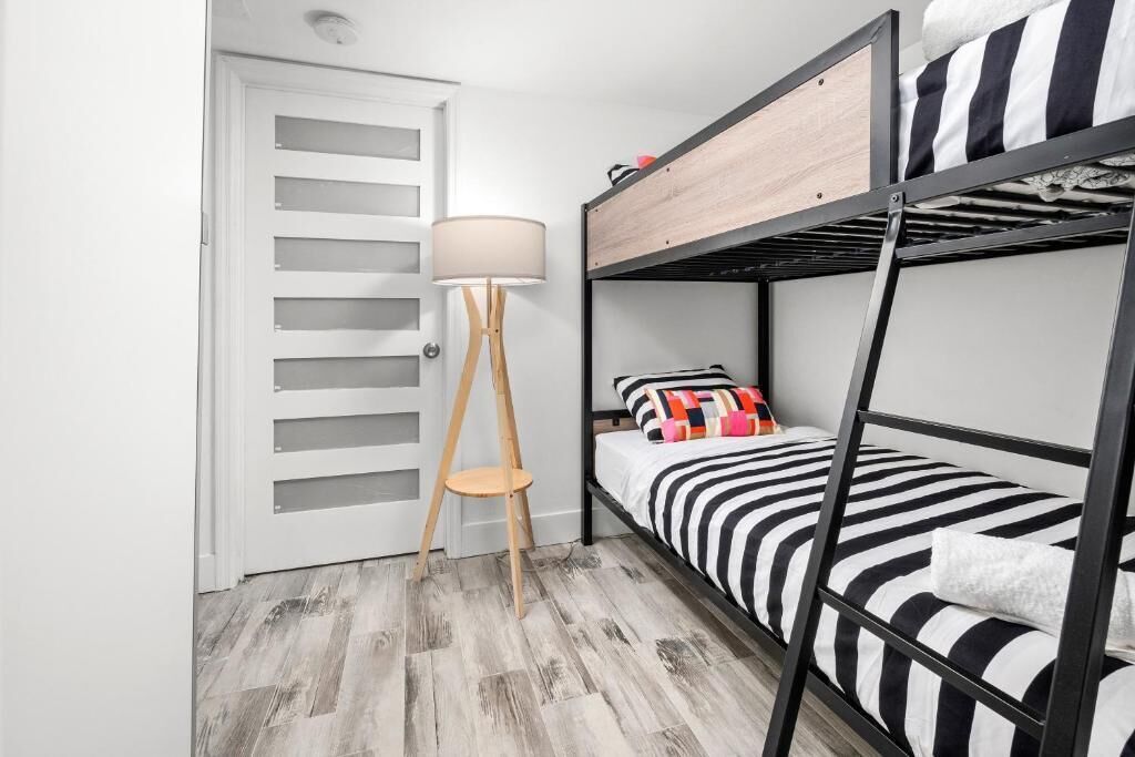 A bunk bed room with a wooden floor, a white door with horizontal slats, and a floor lamp.