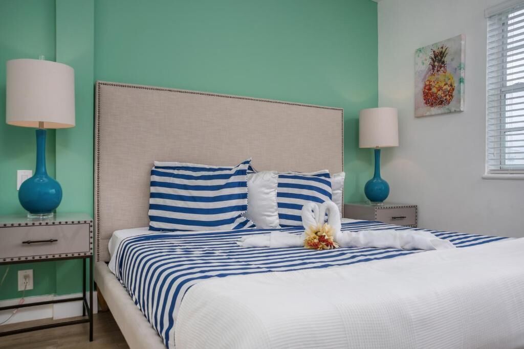A neatly made bed with striped bedding, two bedside lamps, a decorative swan, and a pineapple artwork on the wall.