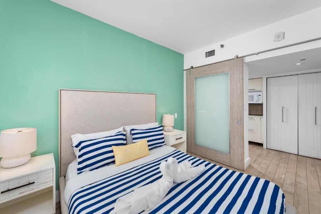 A hotel room with a bed featuring blue and white striped bedding, a wooden headboard, and a white nightstand with a lamp.