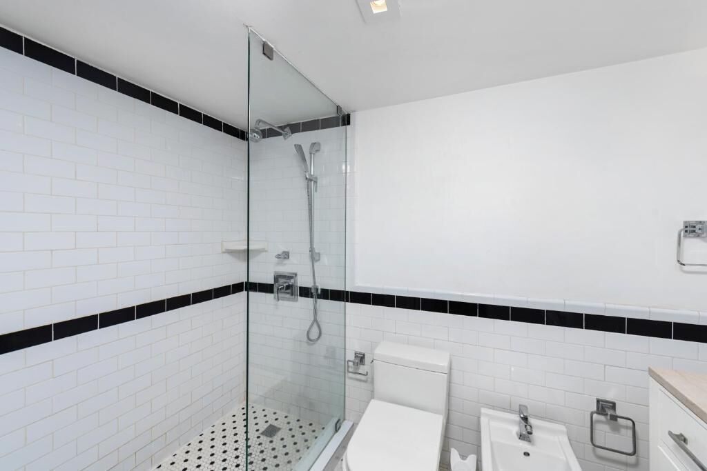 Un baño moderno con azulejos blancos tipo metro, detalles en negro, cabina de ducha de vidrio, inodoro y lavamanos.