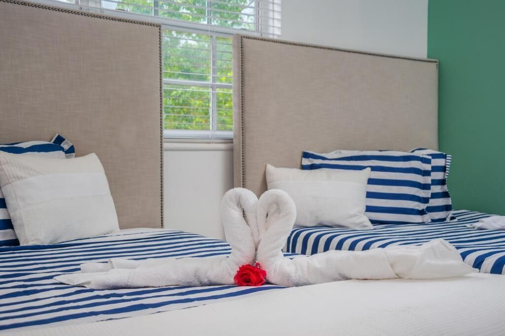 Une chambre d’hôtel avec un lit doté de draps à rayures bleues et blanches, une tête de lit beige et une fenêtre donnant sur un paysage verdoyant.