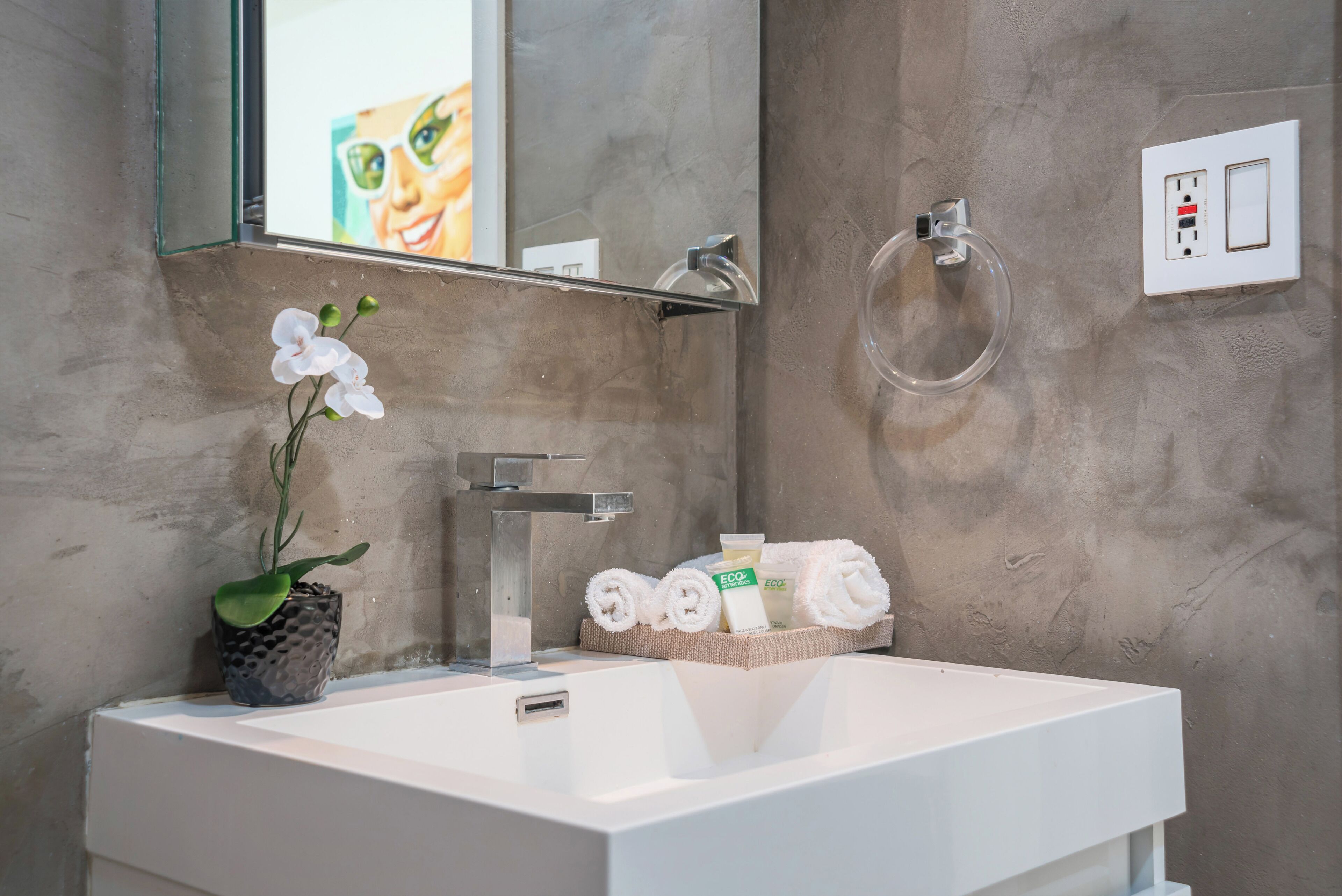 Une salle de bain moderne avec un lavabo blanc, un miroir, une orchidée en pot et des articles de toilette rangés sur une étagère.