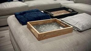 Un salon moderne avec un canapé d’angle gris, un plateau en bois orné d’un motif mandala et un plaid bleu.
