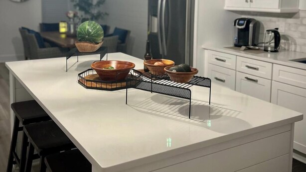 Une cuisine moderne avec des meubles blancs, un îlot central doté de tabourets, des luminaires suspendus et une machine à café.