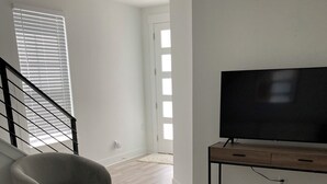 Un salon moderne avec un canapé, un fauteuil, un téléviseur posé sur un meuble en bois et un escalier.