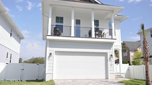 Une maison à deux étages avec un balcon, un garage et une façade blanche.