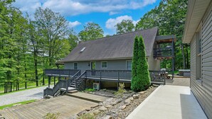 A two-story house with a covered deck, a stone retaining wall, and a gravel driveway. - ‘Shady Point Retreat’ w/ Hot Tub & Pickleball! (Killbuck)